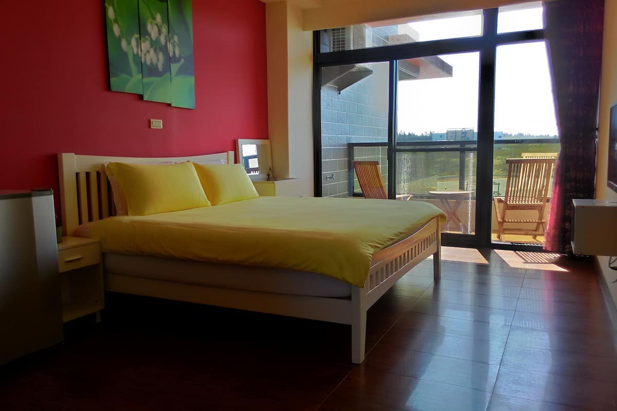 Un dormitorio con cama, mesita de noche, una silla y vistas al exterior a través de un gran ventanal.