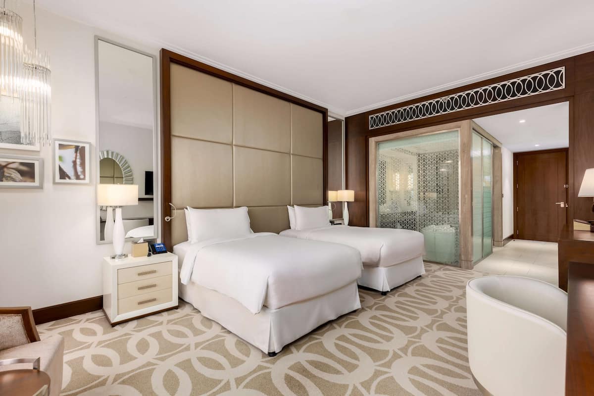 Habitación de hotel con dos camas, una mesita de noche, una silla, un espejo y una alfombra estampada.