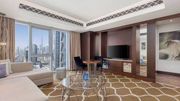 A modern hotel room with a sofa, a glass coffee table, a TV, and a view of the cityscape.