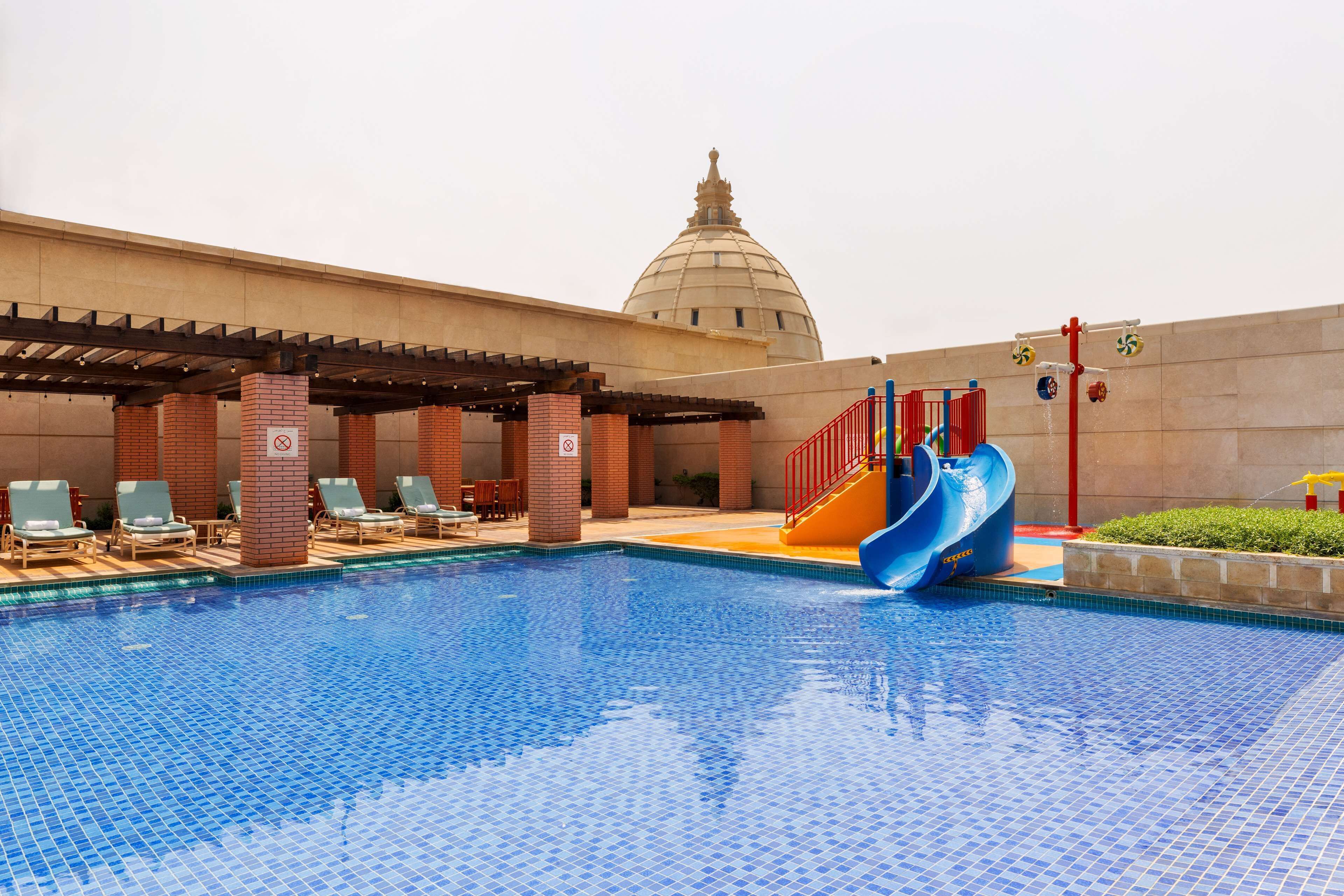 A swimming pool with a blue slide, lounge chairs, and a dome-shaped building in the background.