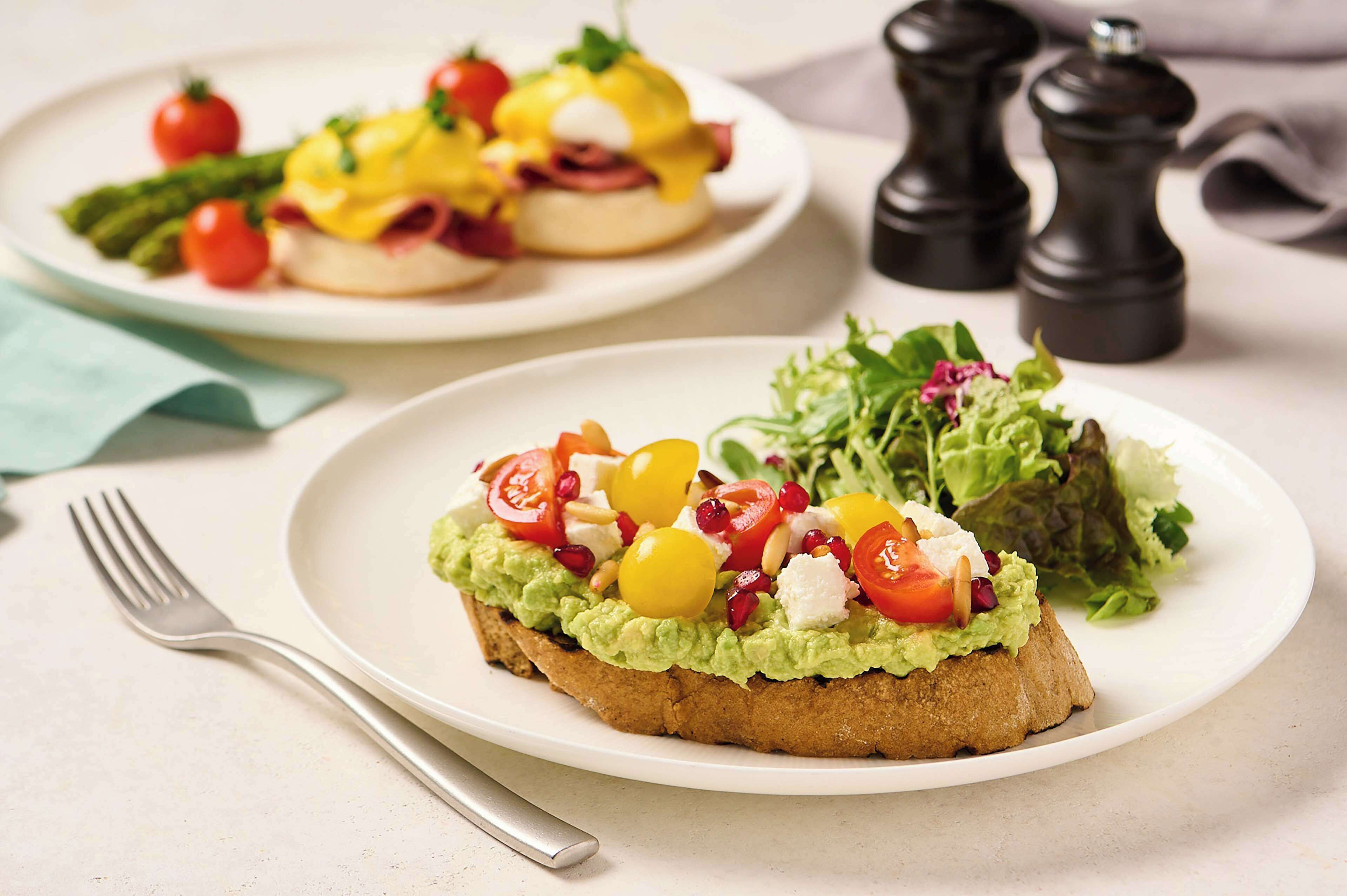 A plate of avocado toast topped with tomatoes, pomegranate seeds, and a side salad.