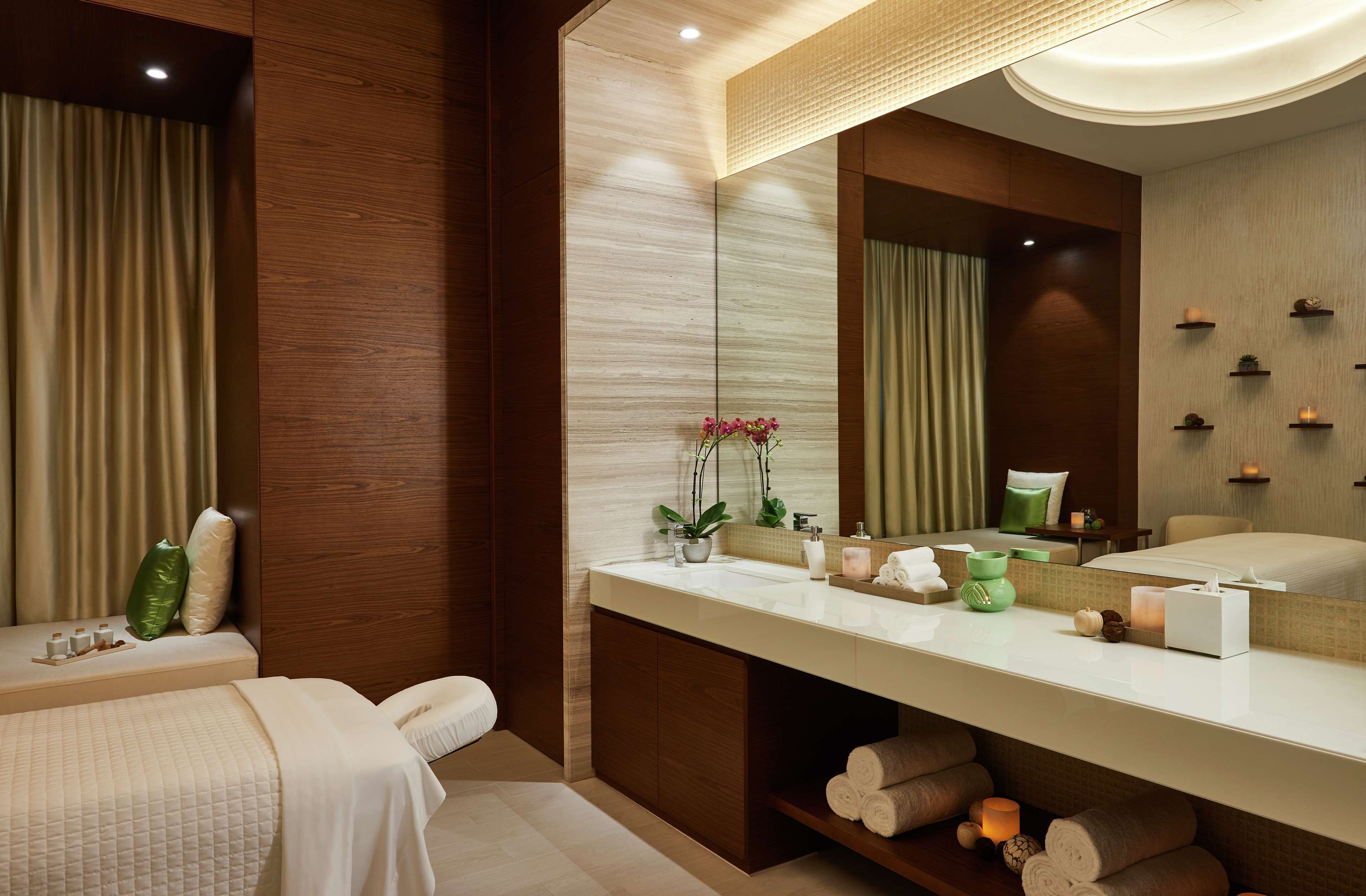 A modern bathroom with a large mirror, wooden paneling, a vanity with toiletries, and a bed with a green pillow.