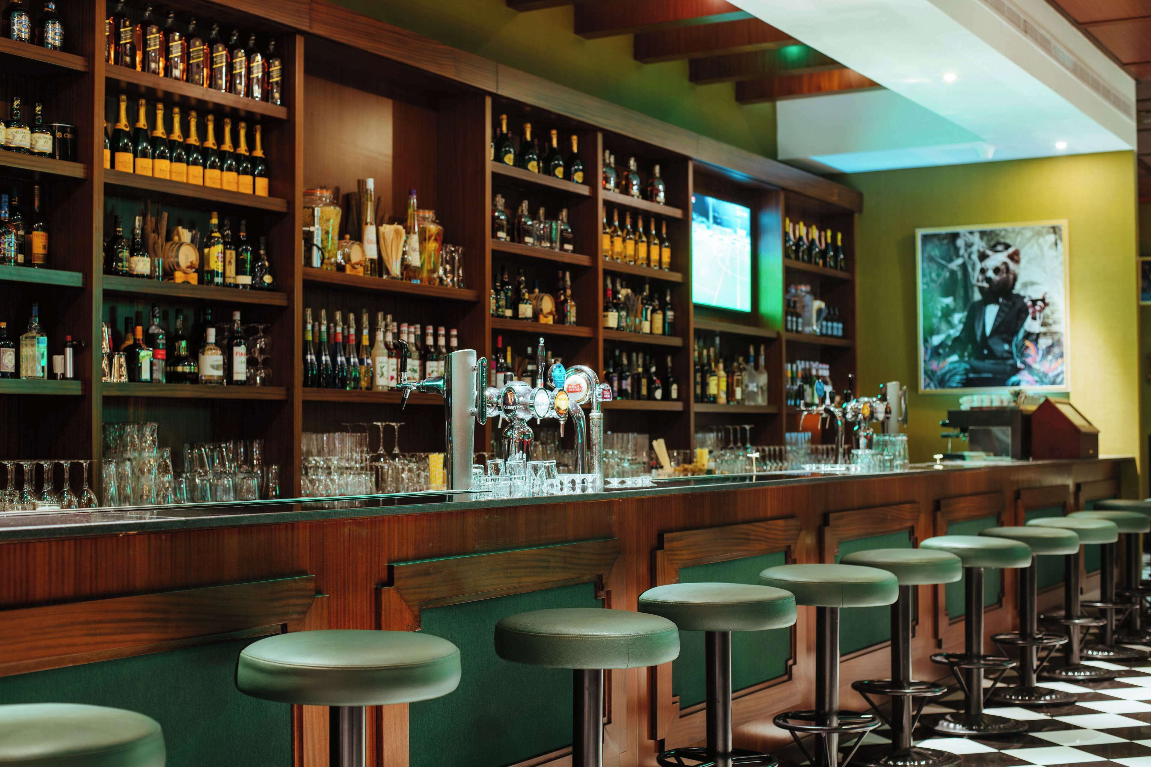 Eine Bar mit mehreren Hockern, Regalen voller Flaschen, Gläsern und einem Fernsehbildschirm.