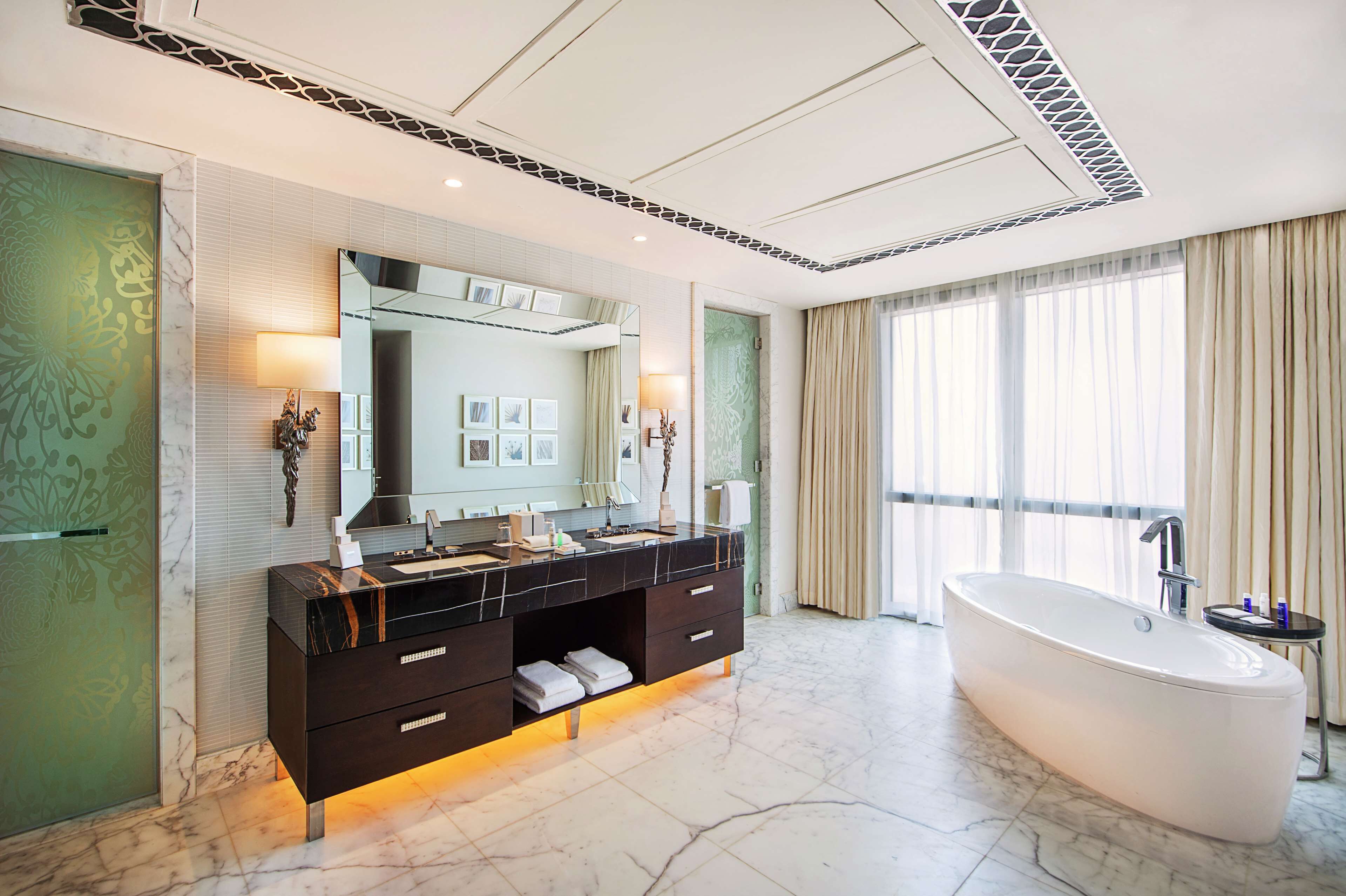 A modern bathroom with a large bathtub, a vanity with a mirror, and a large window with curtains.