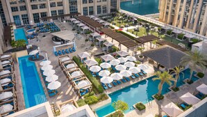 A rooftop pool area with multiple lounge chairs and umbrellas, surrounded by a landscaped garden and a large building in the background. - Hilton Dubai Al Habtoor City (Dubai)