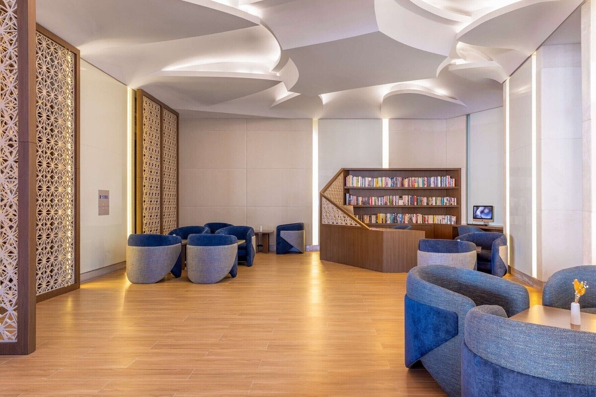 Un área de descanso moderna con piso de madera, asientos azules, una estantería y una escalera.