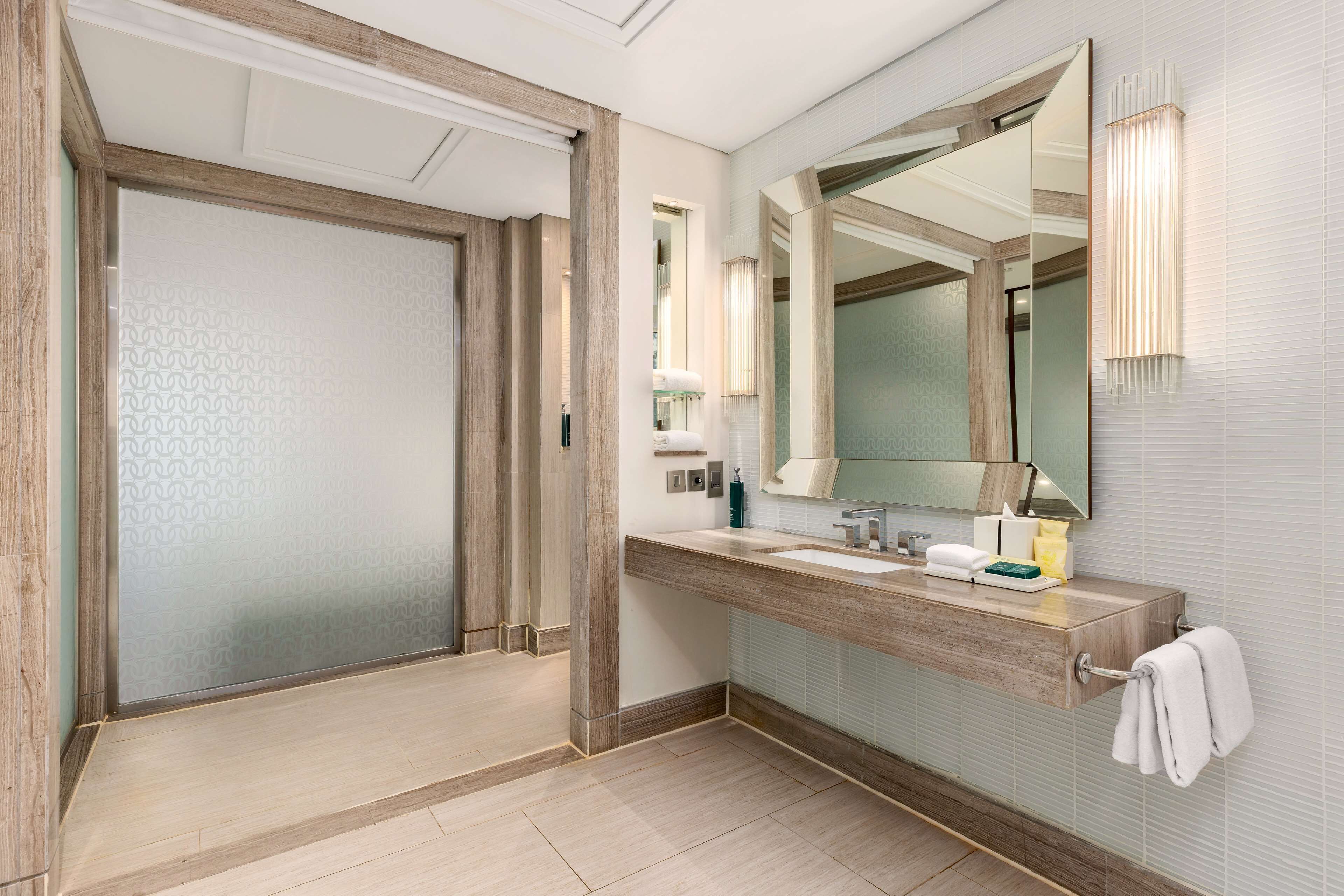 A modern bathroom with a large mirror, wooden vanity, and a towel rack.