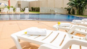 A pool area with white lounge chairs, a small waterfall feature, and a tiled deck. - eSuites Vale dos Carajás (Parauapebas)