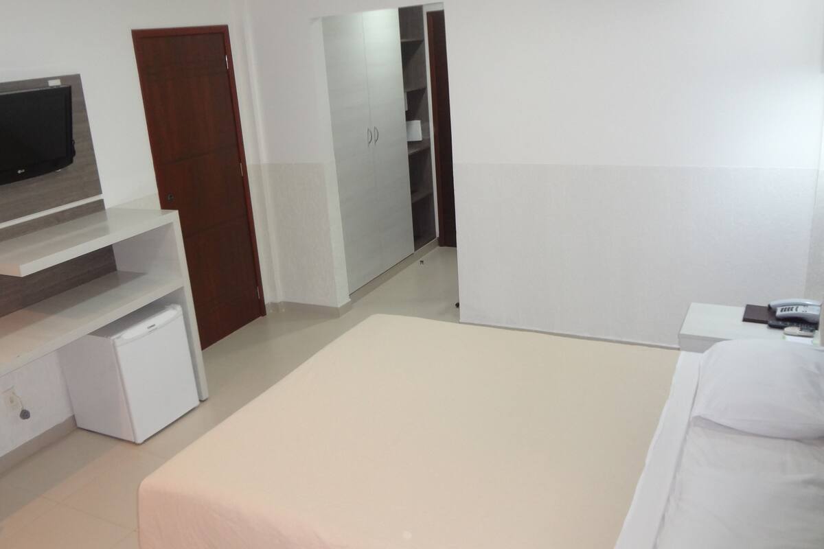 A modern hotel room with a bed, a TV mounted on the wall, a small refrigerator, and a wardrobe.