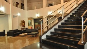 A spacious lobby with a black staircase, a seating area with sofas, and a large mirror. - eSuites Vale dos Carajás (Parauapebas)