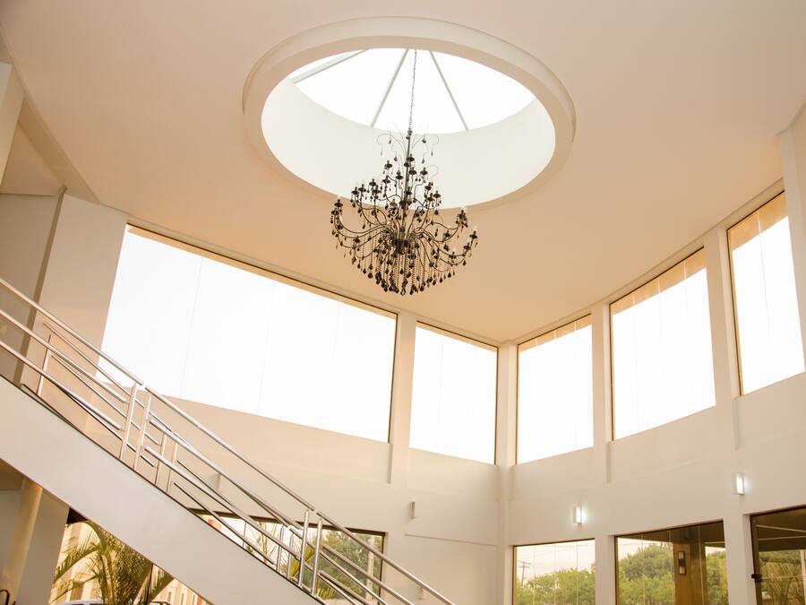A spacious interior with a central chandelier, large windows, and a staircase.