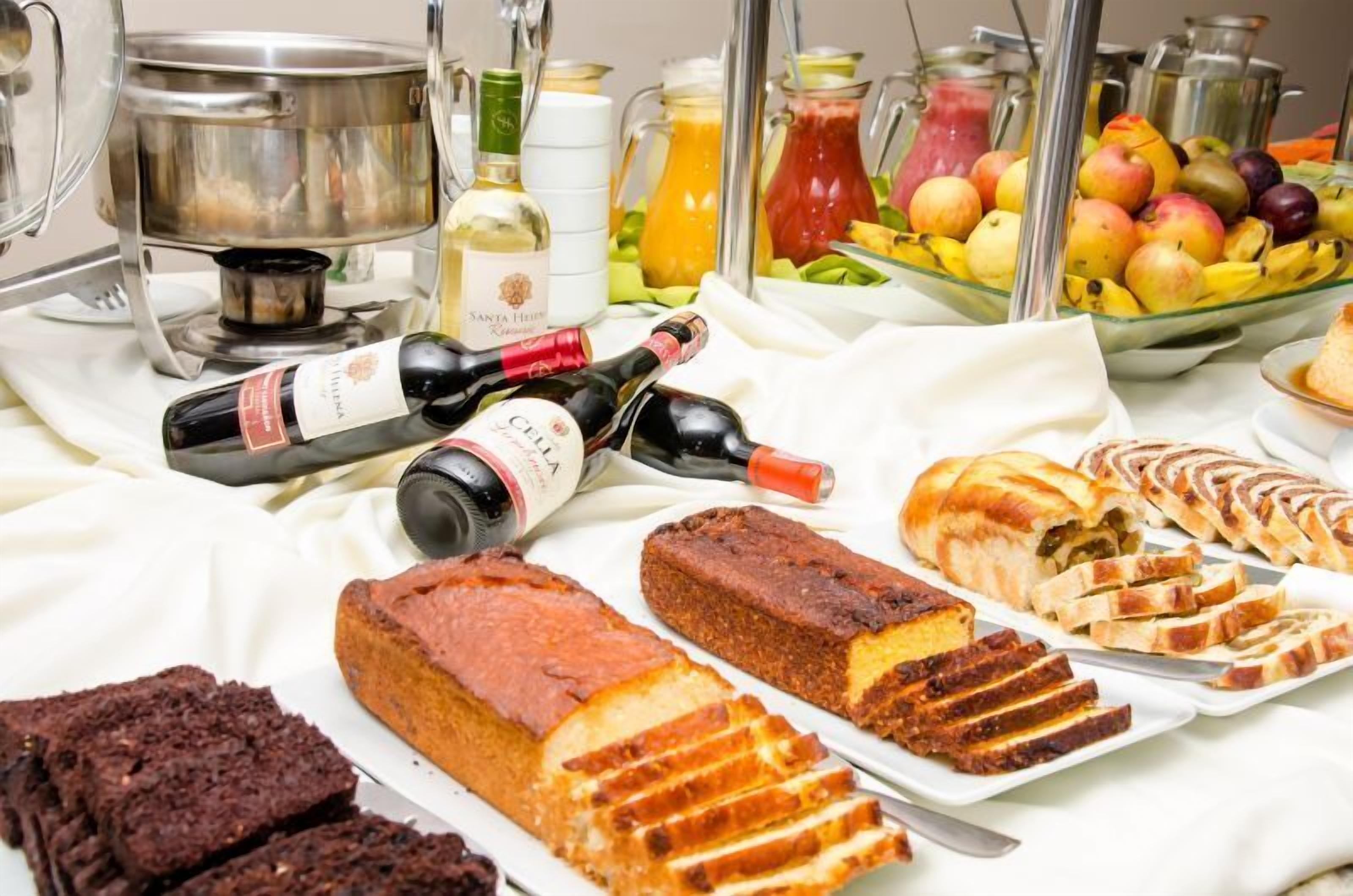 A buffet table with various food items, including bread, cakes, and fruits, along with bottles of wine.