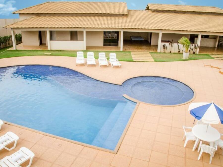 Ein Swimmingpool mit Liegestühlen und einem Tisch mit Sonnenschirm, umgeben von einer überdachten Terrasse.