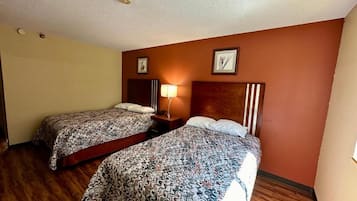 Een hotelkamer met twee bedden, houten vloeren, een plafondlamp en een nachtkastje met een lamp.