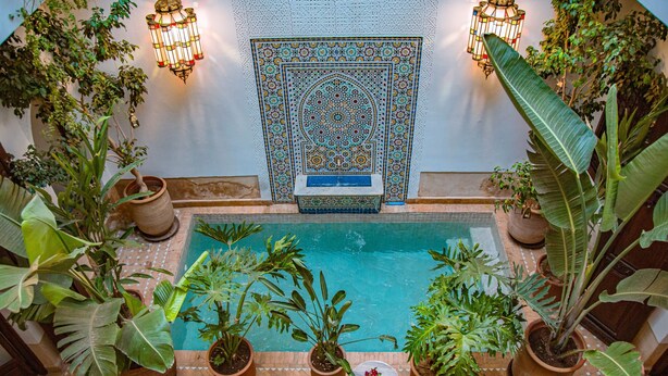 An indoor pool area with potted plants, lounge chairs, and a decorative wall. - Riad Clefs D'orient (Marrakech)