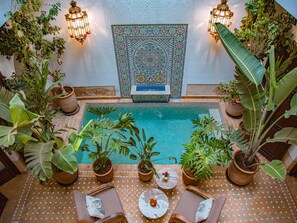 Un espace piscine intérieur agrémenté de plantes en pot, de chaises longues et d’un mur décoratif.