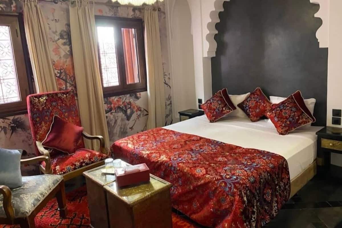 A room with a large bed, a chair, a small table, and curtains.