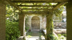 Un sendero de piedra que atraviesa un arco de ladrillo, rodeado de follaje y una pérgola de madera.