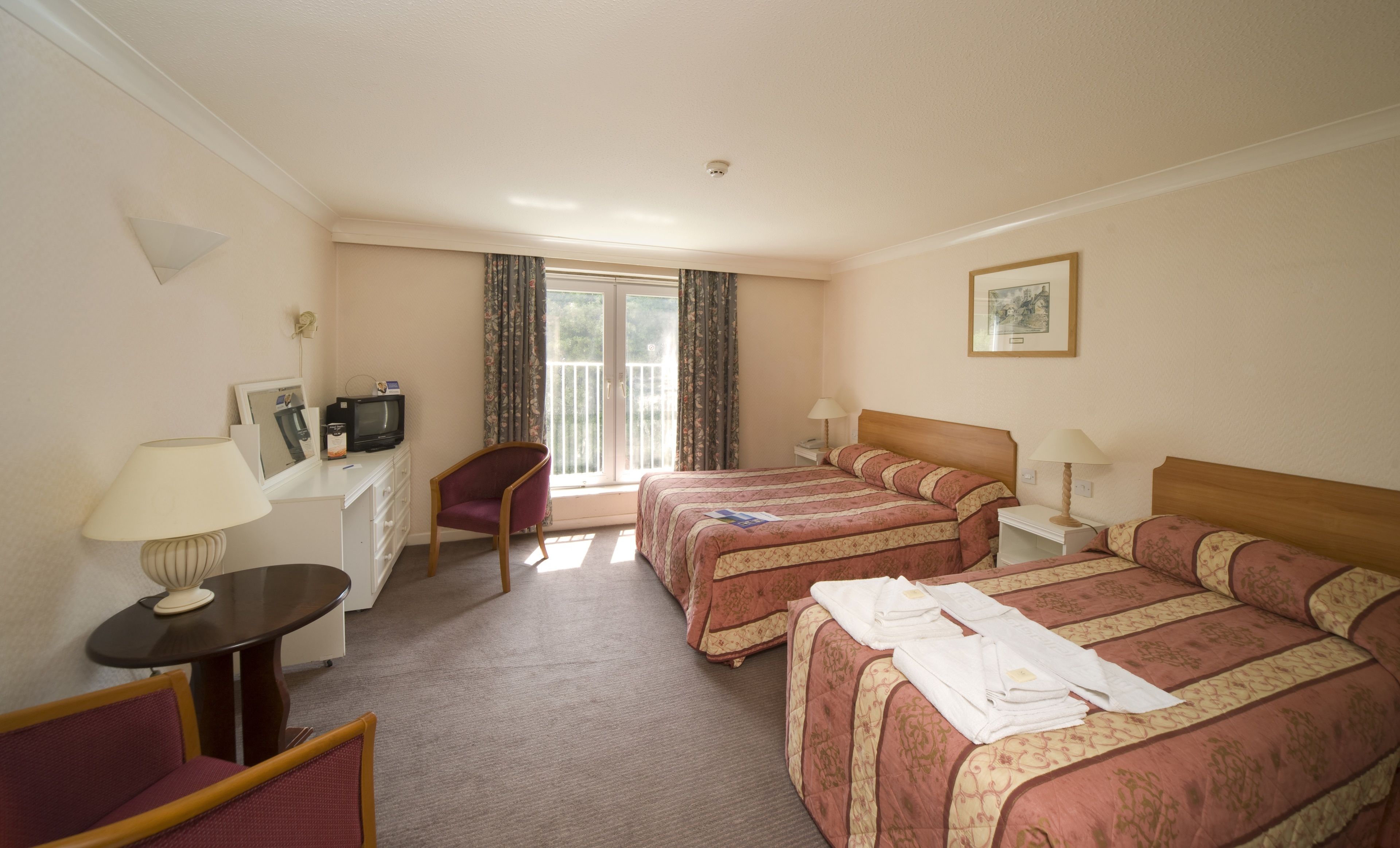 A hotel room with two beds, a desk with a TV, a chair, and a window with curtains.