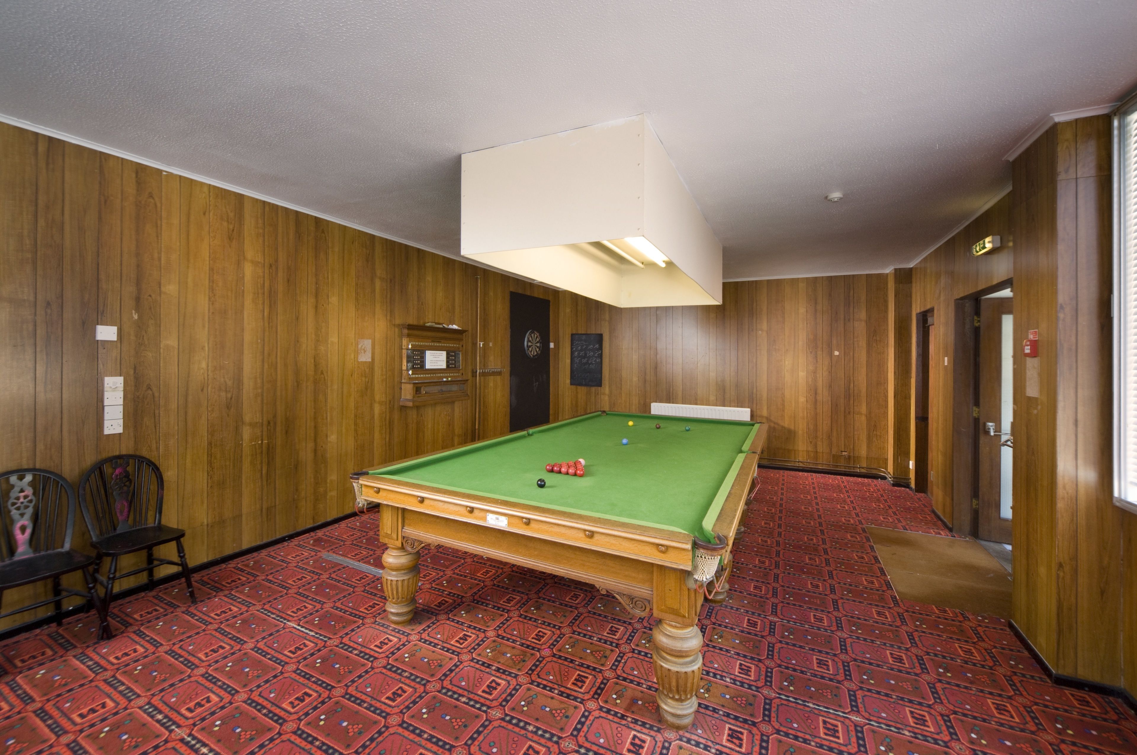 A pool table in a room with wooden paneling and patterned carpet.