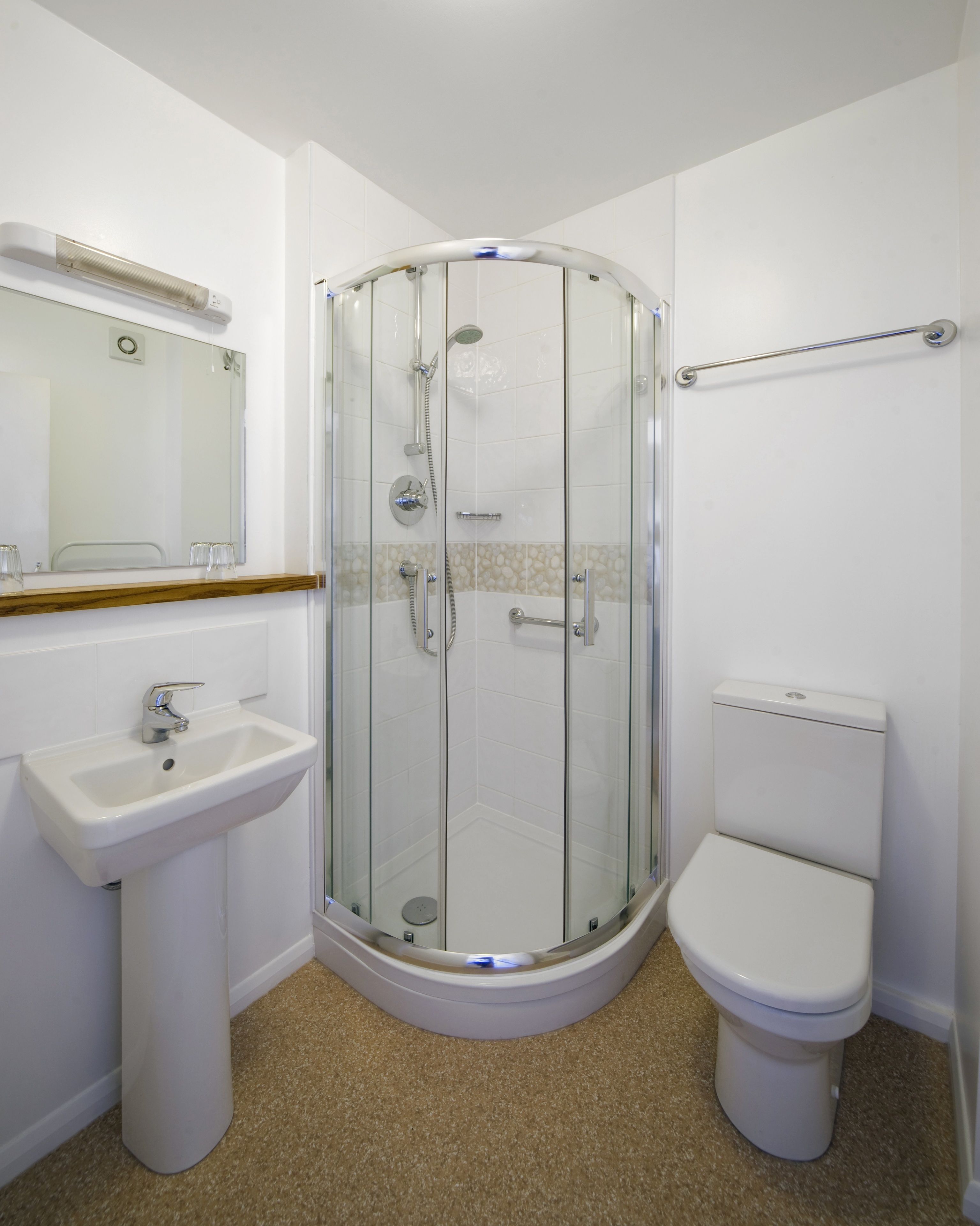 Un baño con ducha de vidrio, lavamanos pedestal y retrete.
