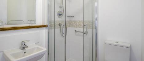 Un baño con ducha de vidrio, lavamanos pedestal y retrete.