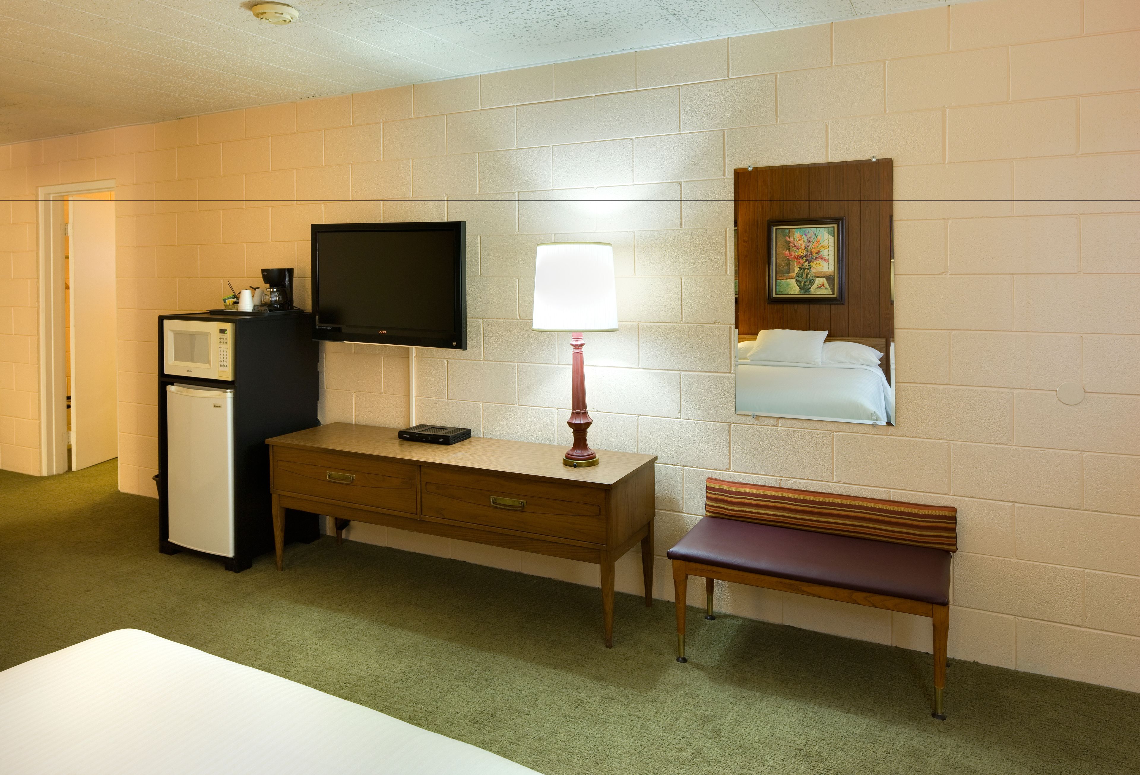 Une petite chambre d’hôtel comprenant un lit, un bureau, une chaise, une télévision, une lampe, un four à micro-ondes et un réfrigérateur.