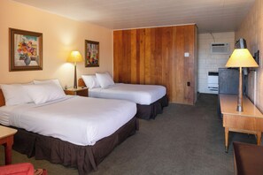 A hotel room with two beds, a desk, a lamp, and a kitchenette.