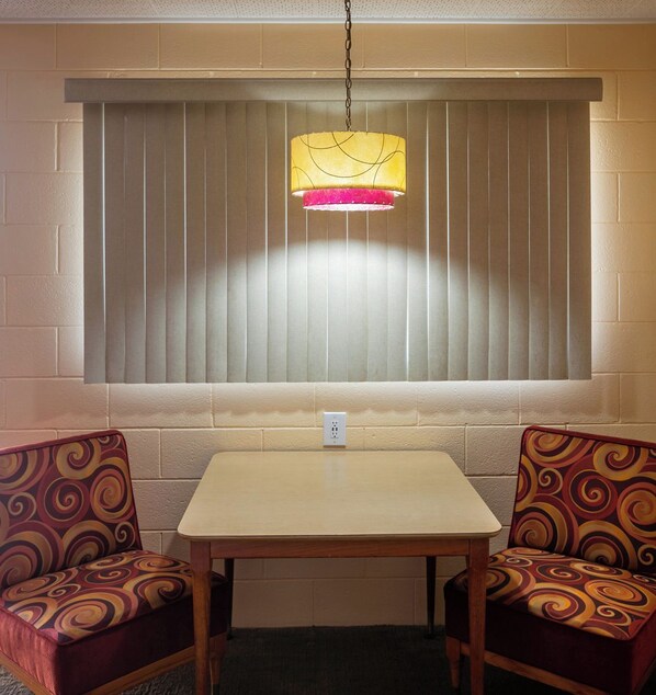 Une pièce avec une table et deux chaises, une fenêtre avec des stores et un luminaire suspendu.