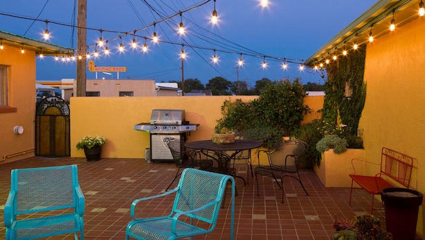 An outdoor patio with a grill, chairs, and string lights. - Sunset Motel (Moriarty)