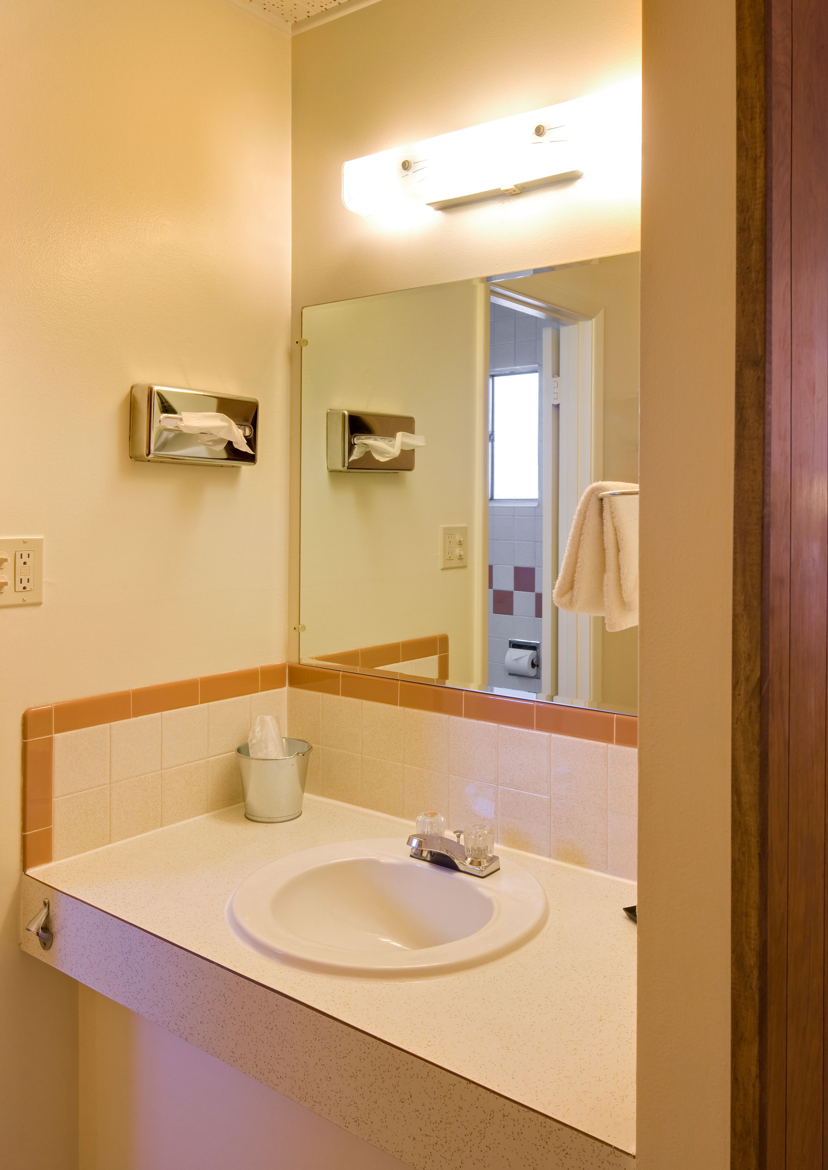 Baño con lavamanos, espejo, dispensador de toallas y una puerta visible que conduce a otra habitación.