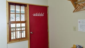 Una habitación con una puerta roja, una ventana con vista a los árboles y un estante de madera.