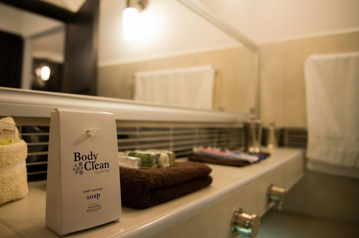 Un baño con encimera blanca, dispensador de jabón para masajes corporales, toalla marrón y un espejo que refleja una toalla.