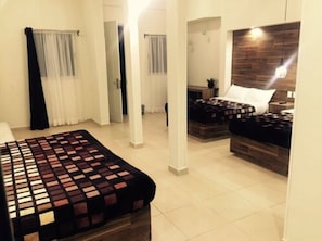 A hotel room with a large bed, two smaller beds, a wooden headboard, a nightstand, and a mirror.