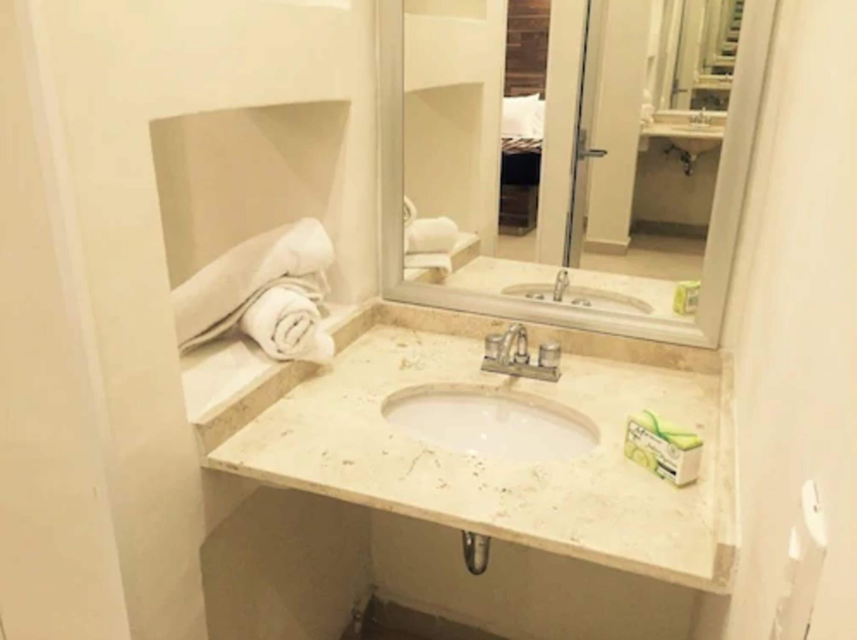 Un baño con lavabo, espejo y perchero para toallas.