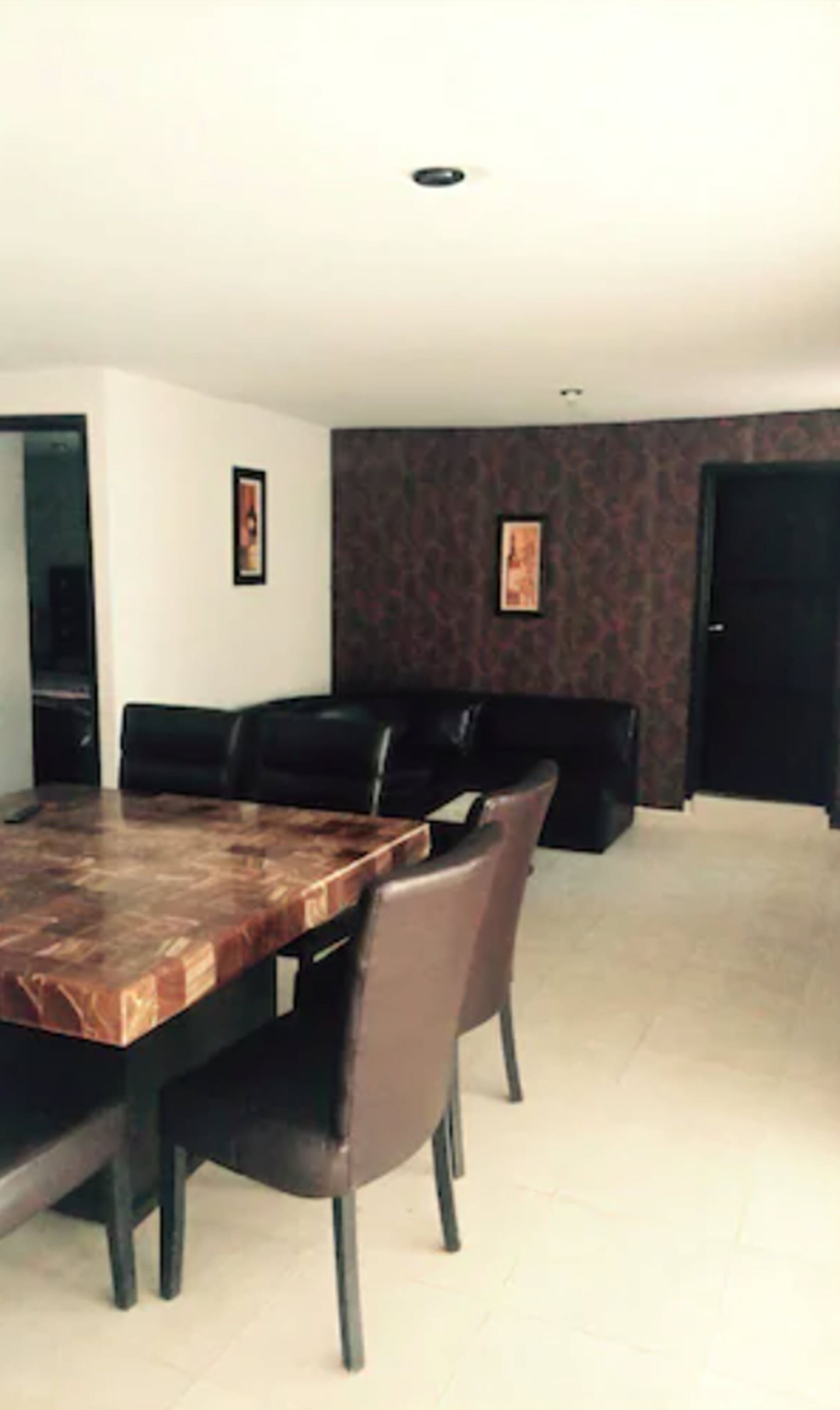 A dining area with a large wooden table, black leather chairs, and a patterned wall.