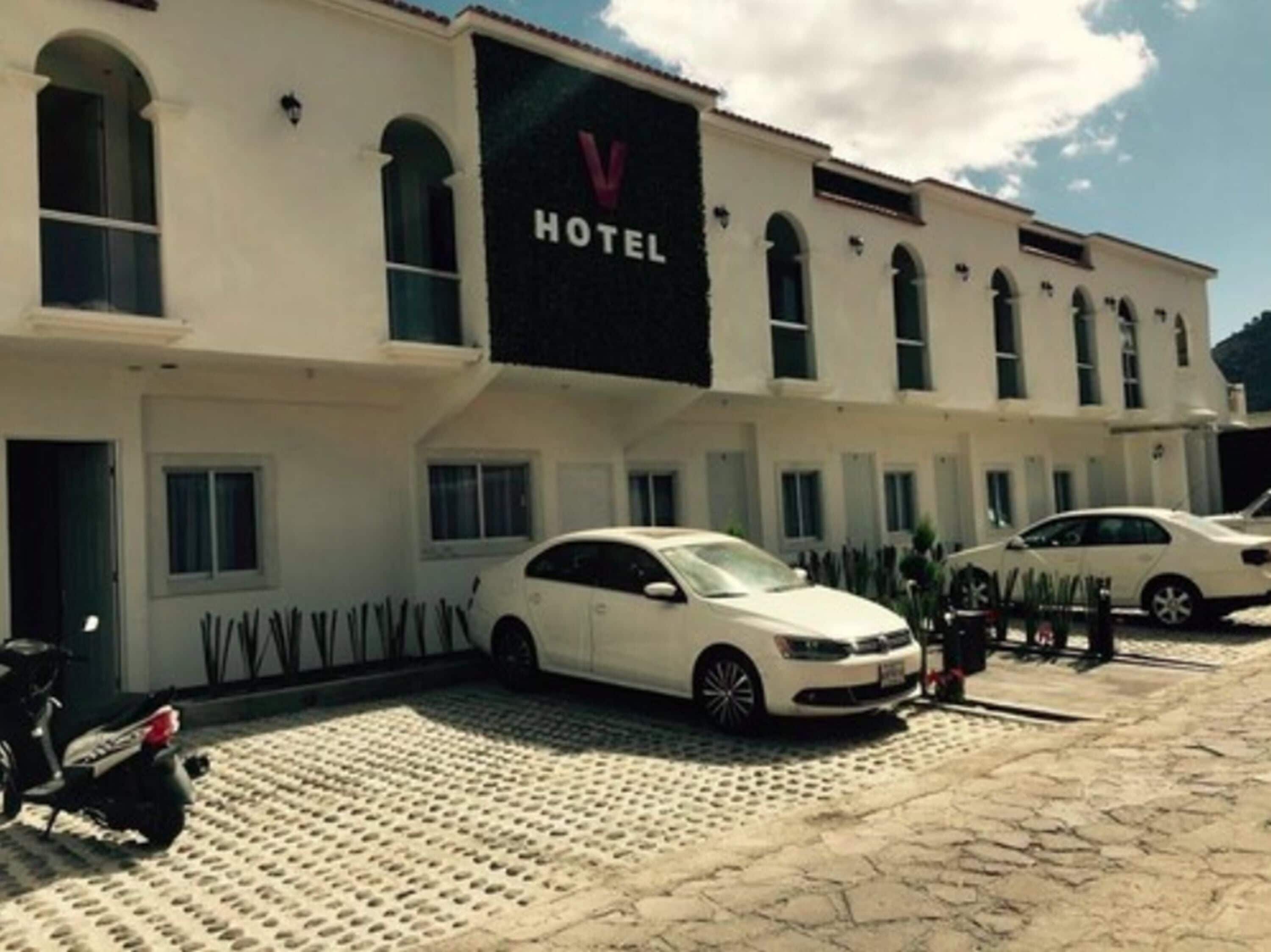 A hotel with a prominent 'HOTEL' sign, a paved courtyard, and parked cars.