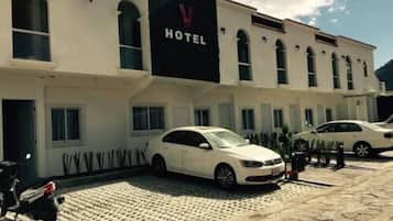 A hotel with a prominent 'HOTEL' sign, a paved courtyard, and parked cars.