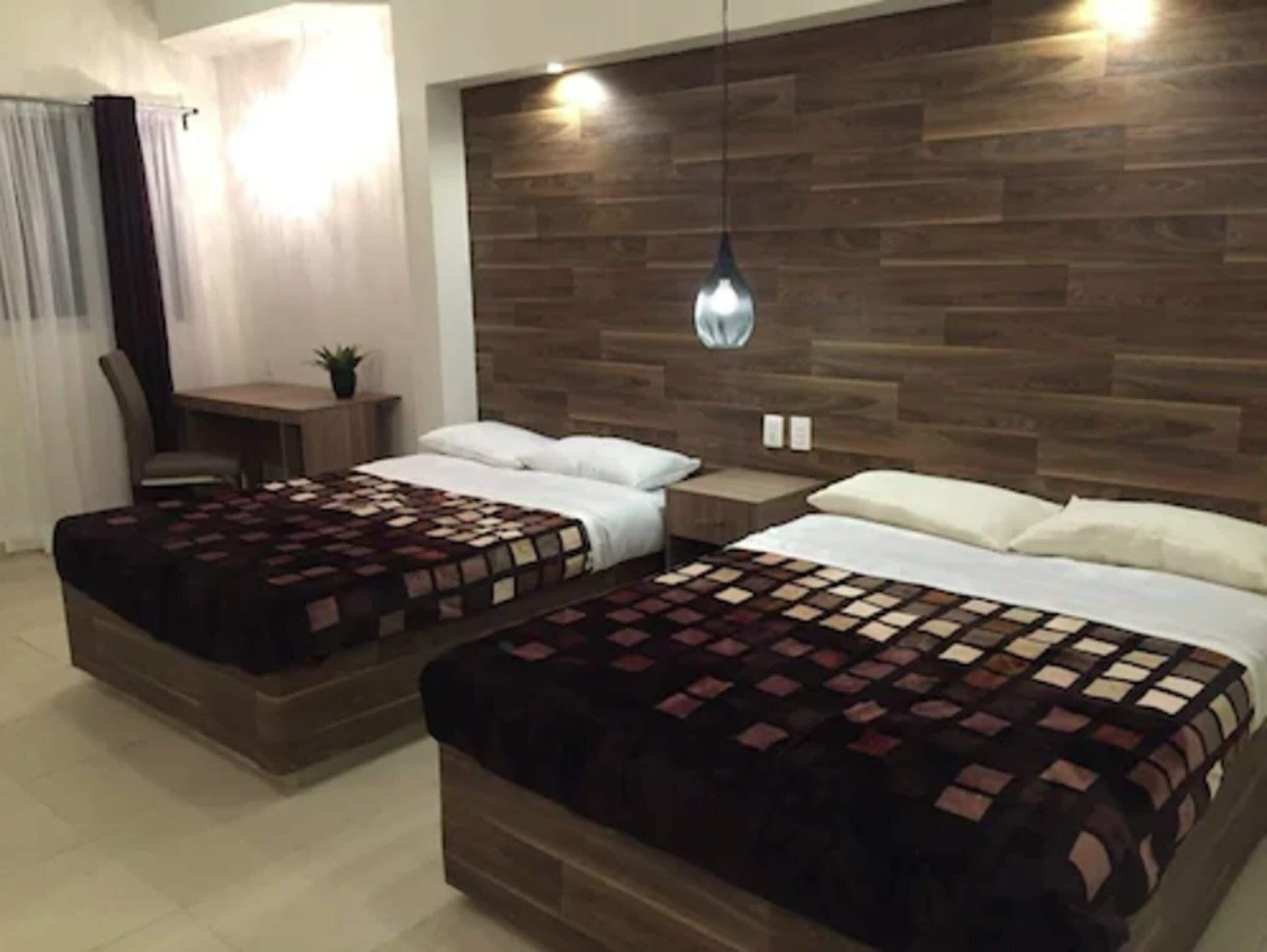 A hotel room with two beds, a desk, and a chair.