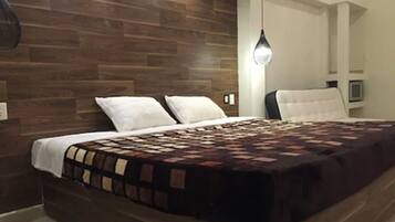 A bedroom with a wooden headboard, a bed with a patterned bedspread, white pillows, and a hanging light fixture.