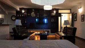 A modern hotel room with a large bed, two sofas, a TV, and a fireplace.