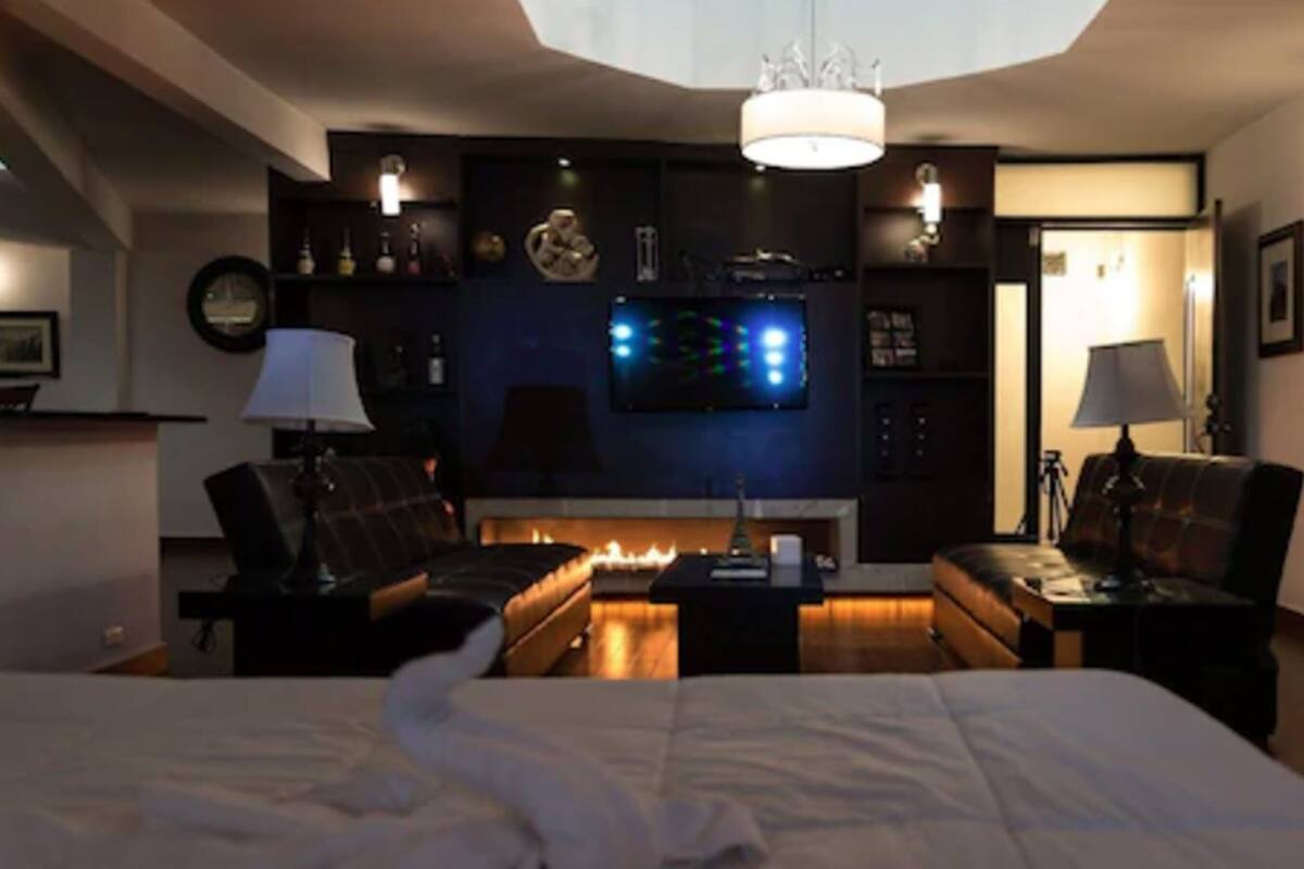 Une chambre d’hôtel moderne avec un grand lit, deux canapés, une télévision et une cheminée.