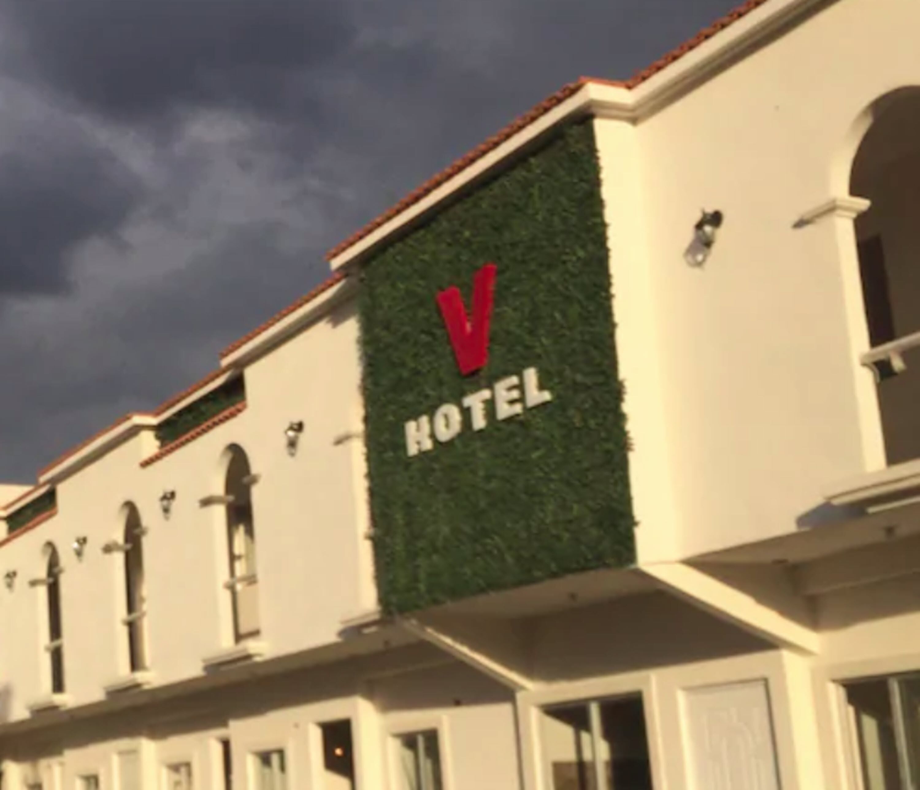 A hotel with a prominent 'V HOTEL' sign on a green wall.
