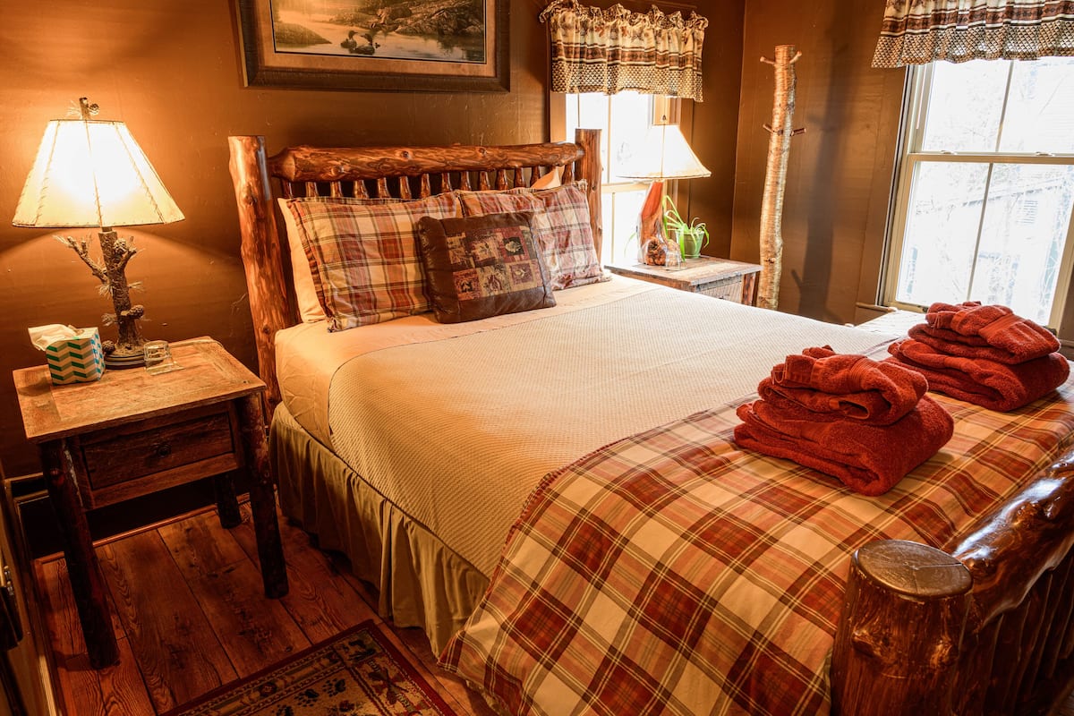 A cozy bedroom with a wooden headboard, a plaid bedspread, and a stack of red towels on the bed.