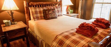 Een gezellig slaapkamer met een houten hoofdeinde, een geruit sprei en een stapel rode handdoeken op het bed.