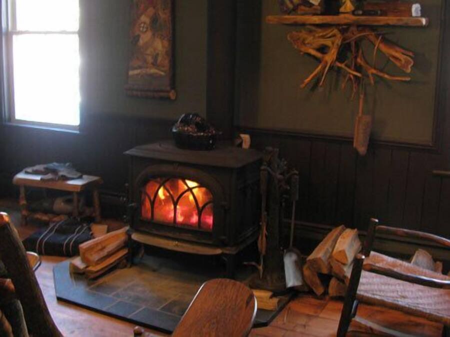 A cozy room with a wood-burning stove, a chair, a small table, and a window.