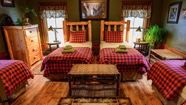 A room with two beds, a wooden dresser, a small table, and a rug with a bear design. - RoosterComb Inn (Keene Valley)
