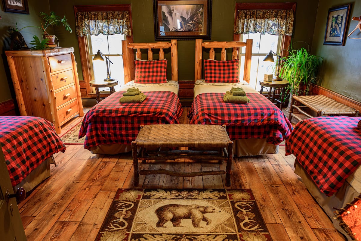 A room with two beds, a wooden dresser, a small table, and a rug with a bear design.