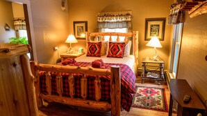 A cozy bedroom with a wooden bed, two bedside tables with lamps, a patterned rug, and a wooden bench. - RoosterComb Inn (Keene Valley)