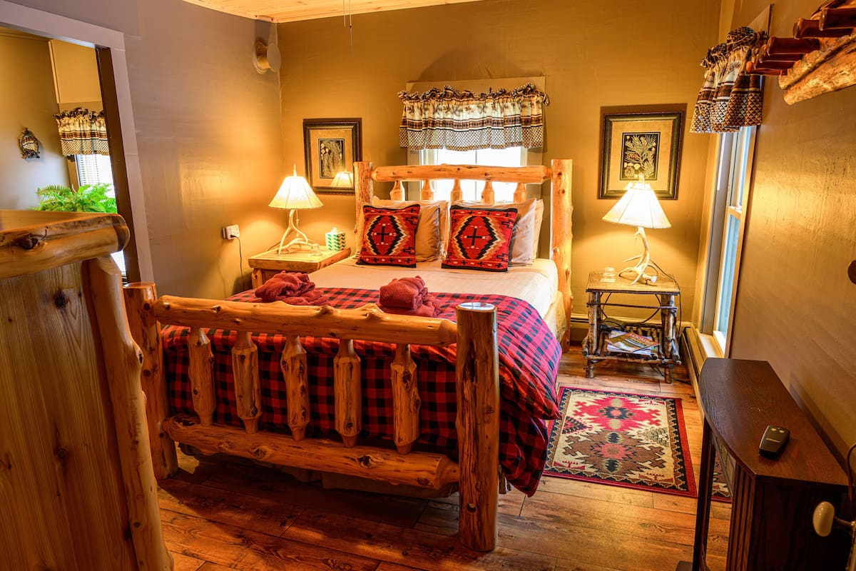 A cozy bedroom with a wooden bed, two bedside tables with lamps, a patterned rug, and a wooden bench.